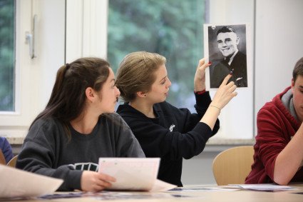 In einem Seminar zeigt eine Schülerin auf ein historisches Porträtfoto, auf dem ein lächelnder Mann zu sehen ist.