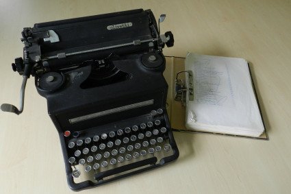 Eine alte, schwarze Schreibmaschine aus Metall und ein Papiermanuskript daneben.