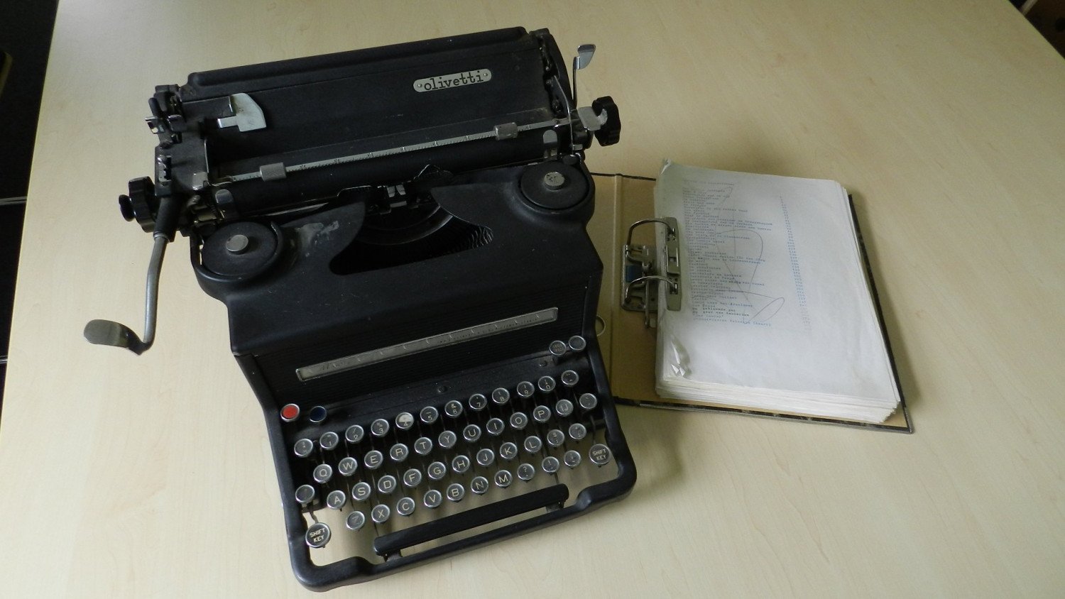 Eine alte, schwarze Schreibmaschine aus Metall und ein Papiermanuskript daneben. 
