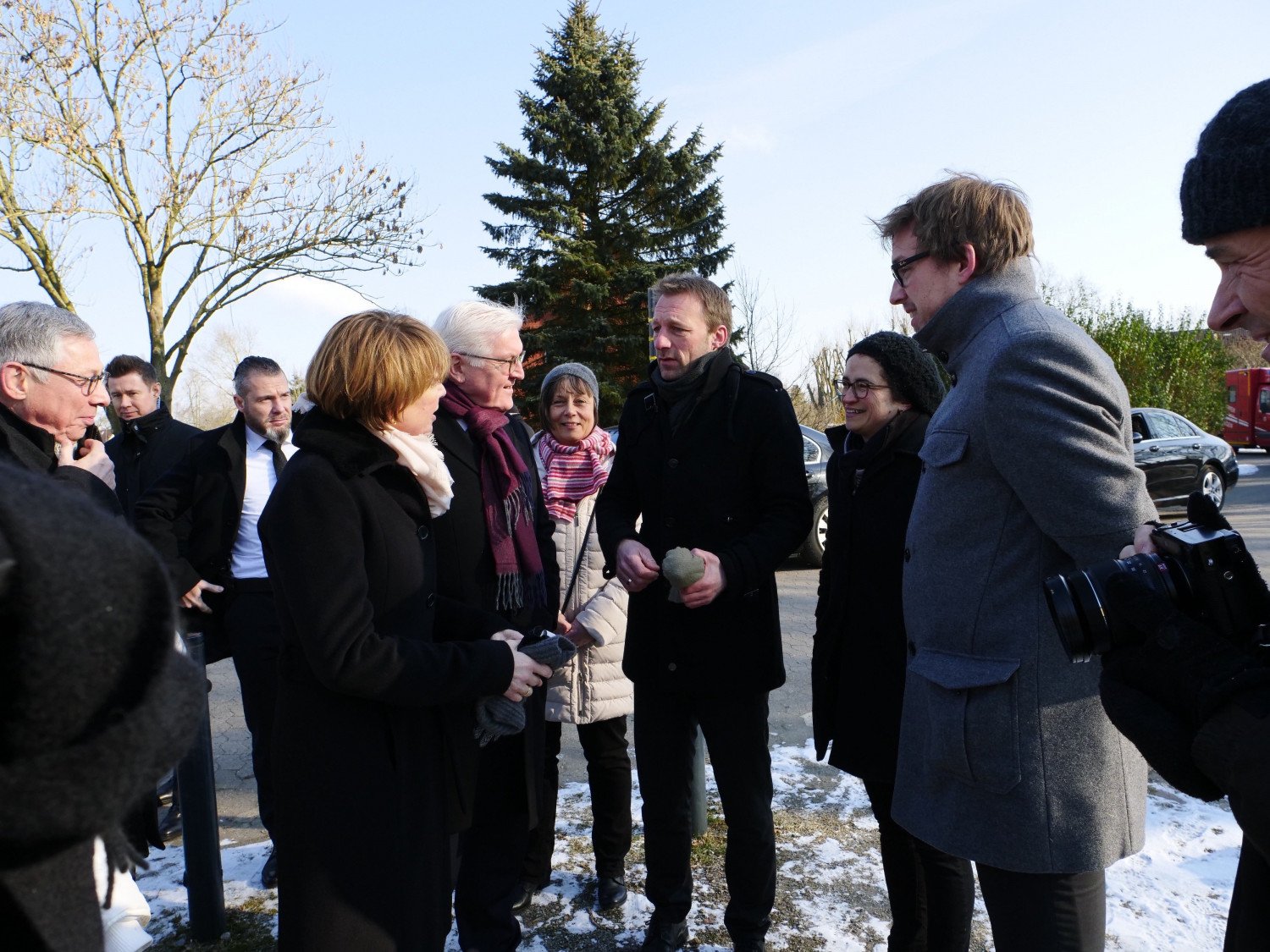 Herr Steinmeier und seine Frau werden von Mitarbeitenden des Denkortes begrüßt. Das Bild ist draußen aufgenommen. Alle stehen und tragen winterliche Bekleidung.  