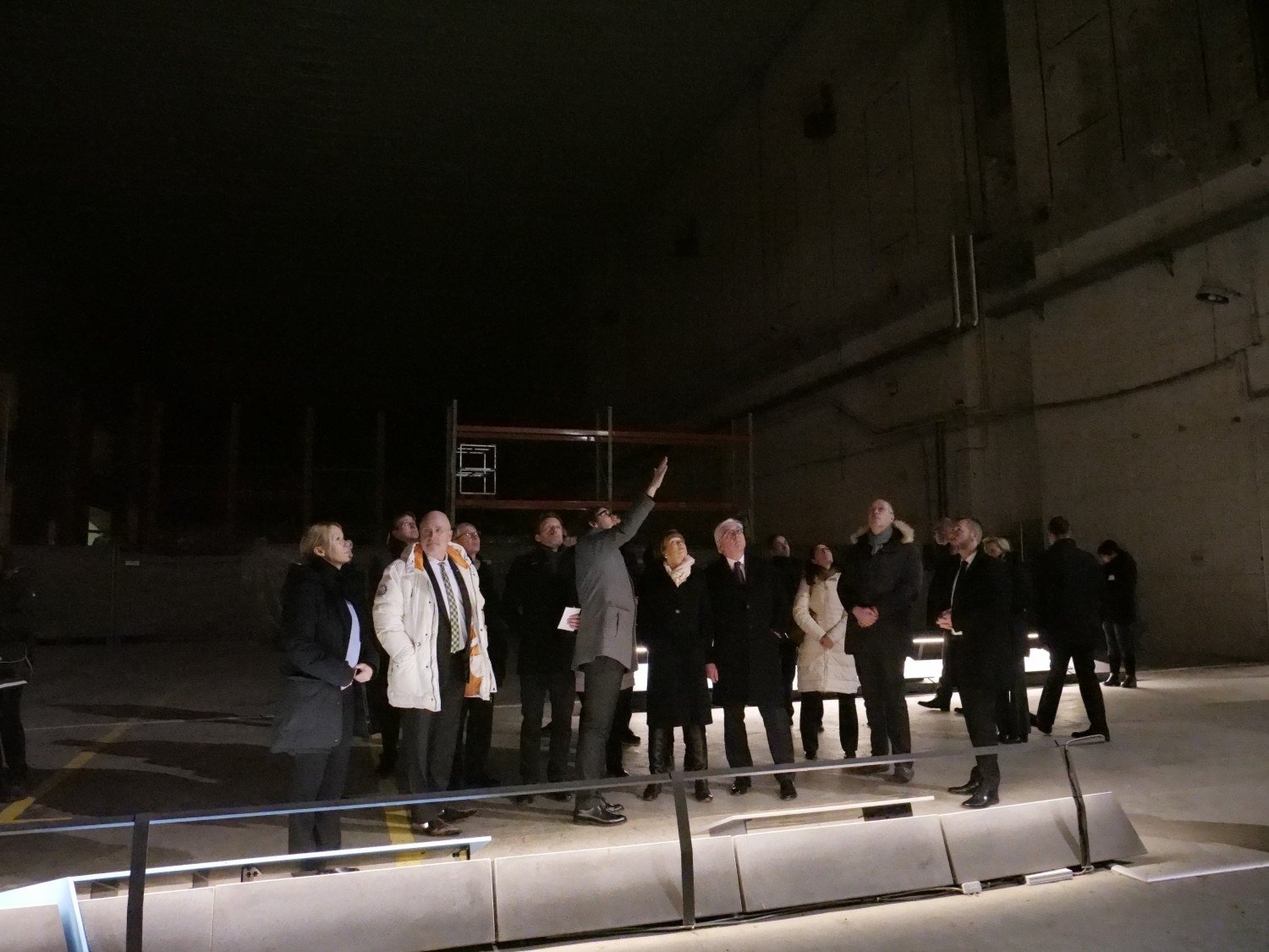 Eine Gruppe von Menschen blickt an die dunkle Bunkerdecke. Nur der Fußboden ist beleuchtet. 