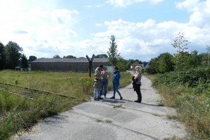 Vier Menschen stehen in einer dörflichen Gegend auf nicht mehr genutzten Bahnschienen.