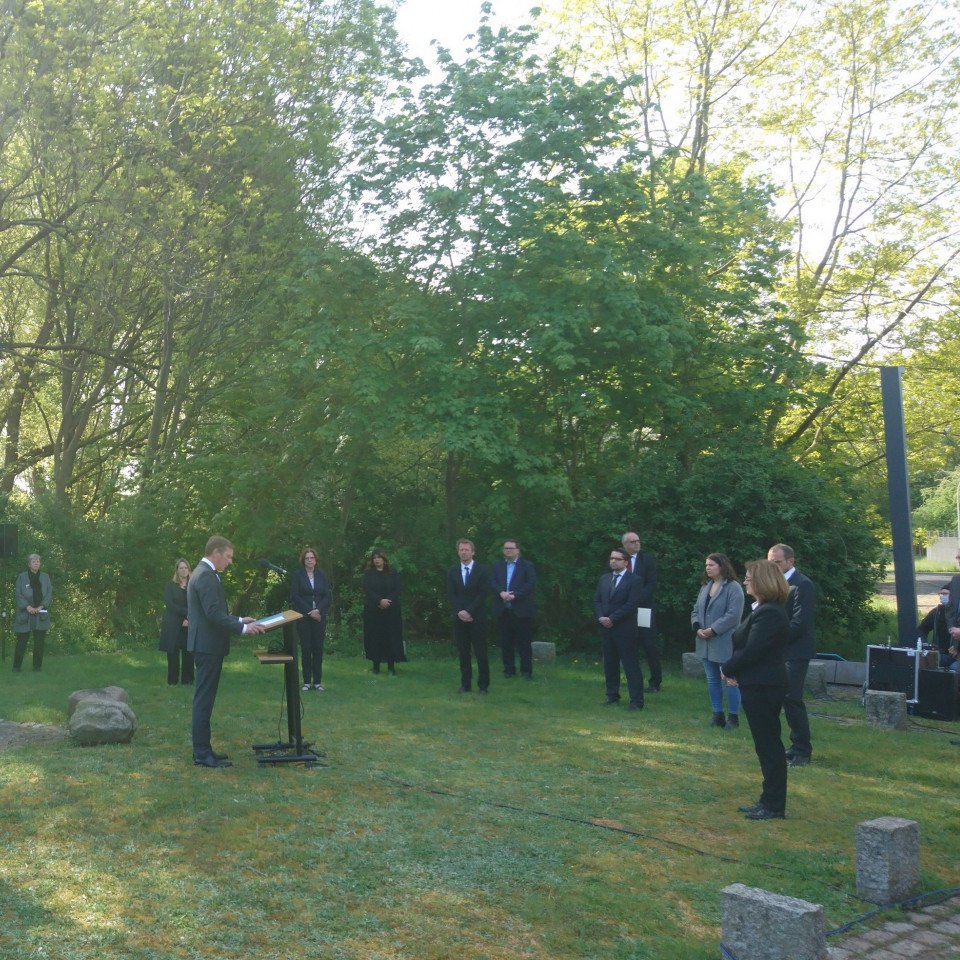 Menschen in schwarzer Kleidung stehen andächtig in einem Halbkreis vor dem Mahnmal "Vernichtung durch Arbeit". Am Rednerpult steht Frank Imhoff, Präsident der Bremischen Bürgerschaft.