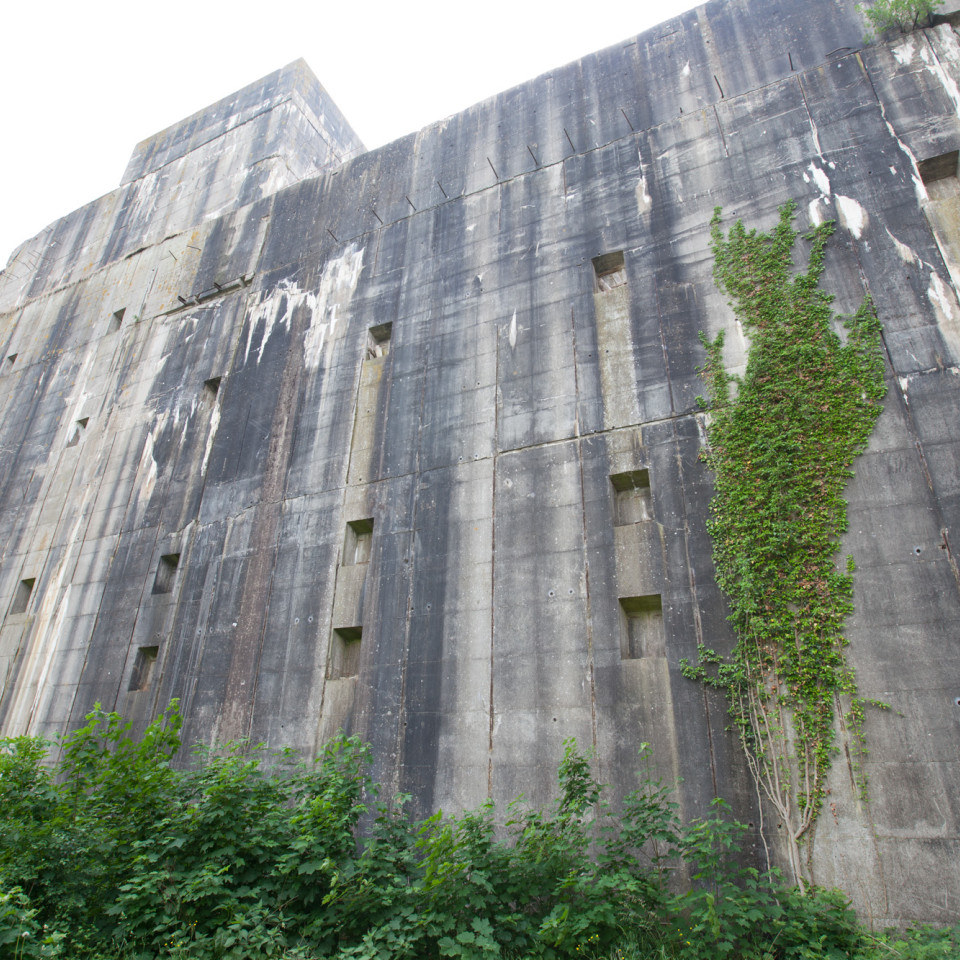 Außenseite des Bunkers, bestehend aus Beton, teileweise mit Kletterpflanzen begrünt.