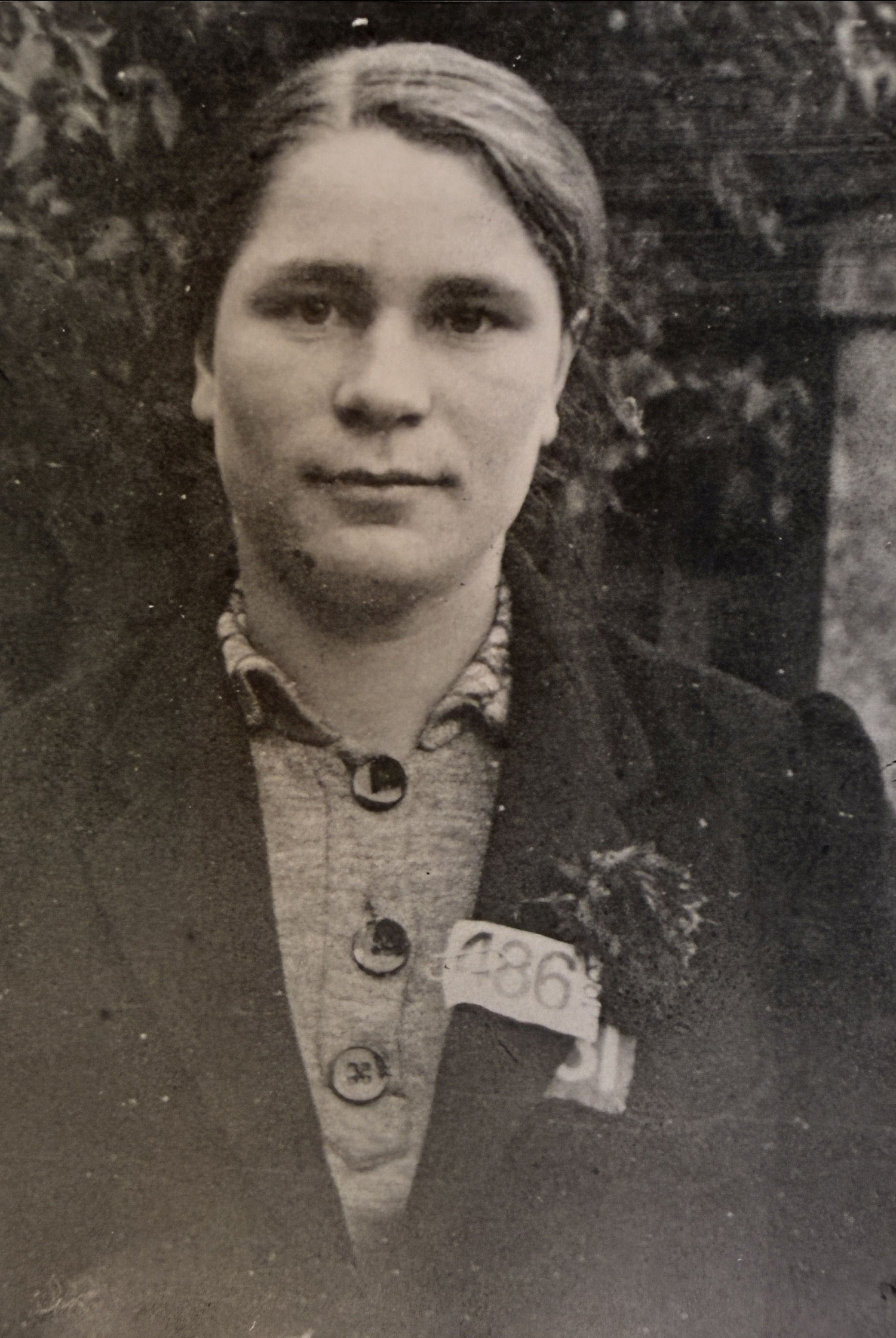Eine junge Frau in einem schwarzen Kleid mit einem Blumenanhänger und einer Karte mit der Nummer 486 an ihrem Kragen. Sie blickt direkt in die Kameralinse. 