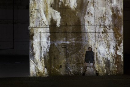 Tanz einer Solokünstlerin. Im Hintergrund wird die Bunkerwand mit Grau- und Weiss-Tönen beleuchtet.