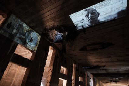 Bildprojektion an die Decke im Ruinenteil. Zu sehen ist das Gesicht einer Person. Schwarz-Weiss-Aufnahme.