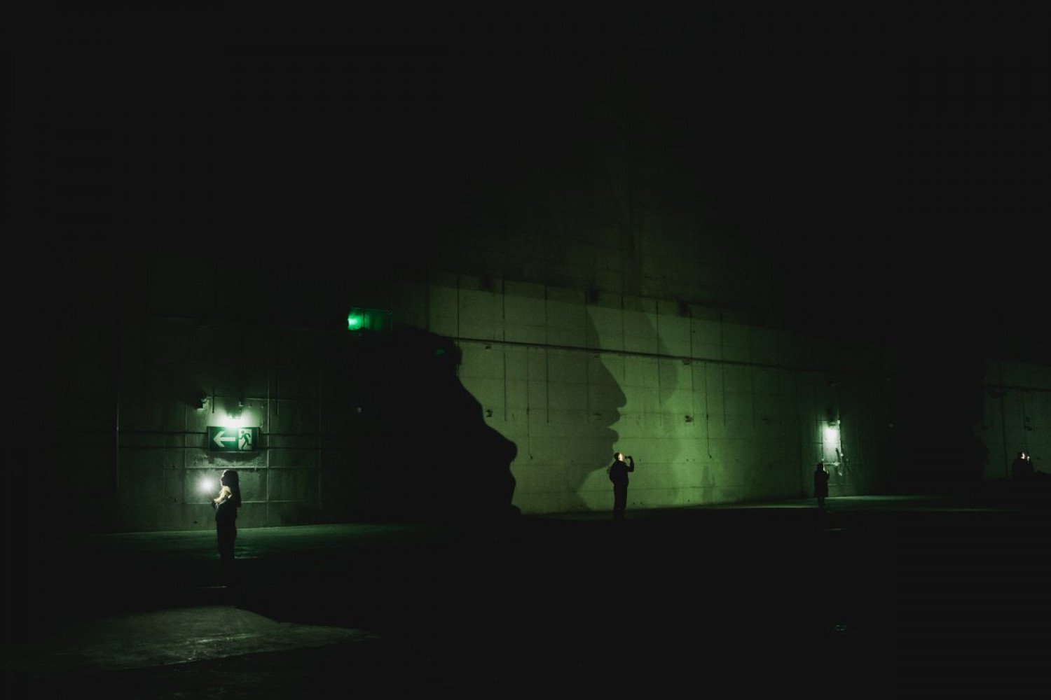 Ein Gesicht wirft einen großen Schatten auf die Bunkerwand im Innenraum. Es ist dunkel. Nur wenig Licht ist im Raum.  