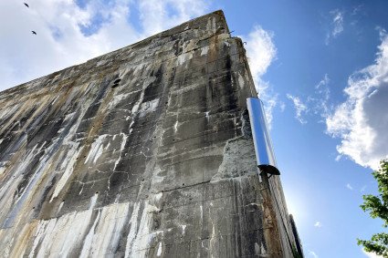 An der Außenwand des Bunker "Valentin" hängt eine Windharfe, sie sieht aus wie ein länglicher Kasten aus silbernem Metall