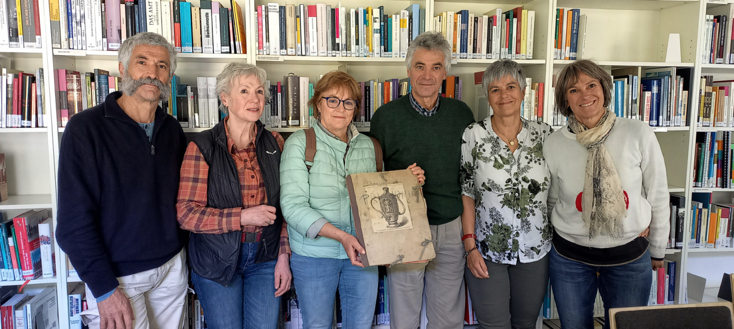 Sechs Personen stehen vor einem Bücherregal und halten eine Zeichnung in den Händen. 