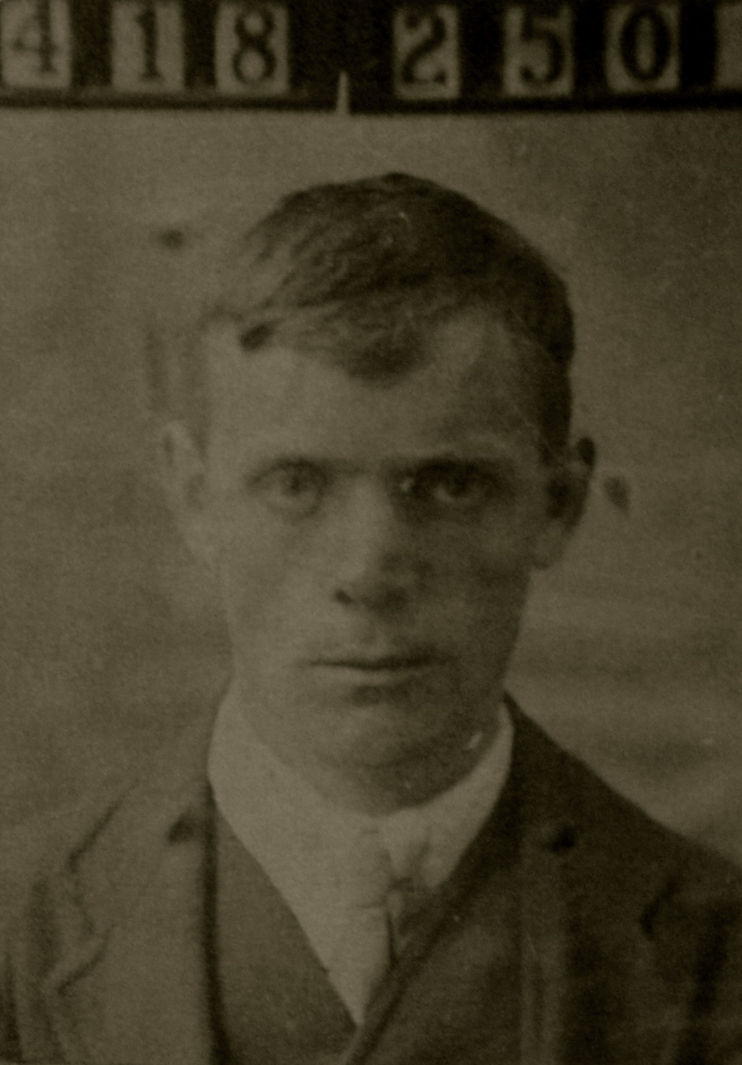 Gezeigt wird ein sepiafarbenes Portrait von einem Mann mit kurzen, dunkelblonden Haaren. Es handelt sich um William Knott. Er trägt einen Anzug mit Krawatte und über ihm steht eine Nummer, 418 250, was für ein Polizeifoto spricht.  