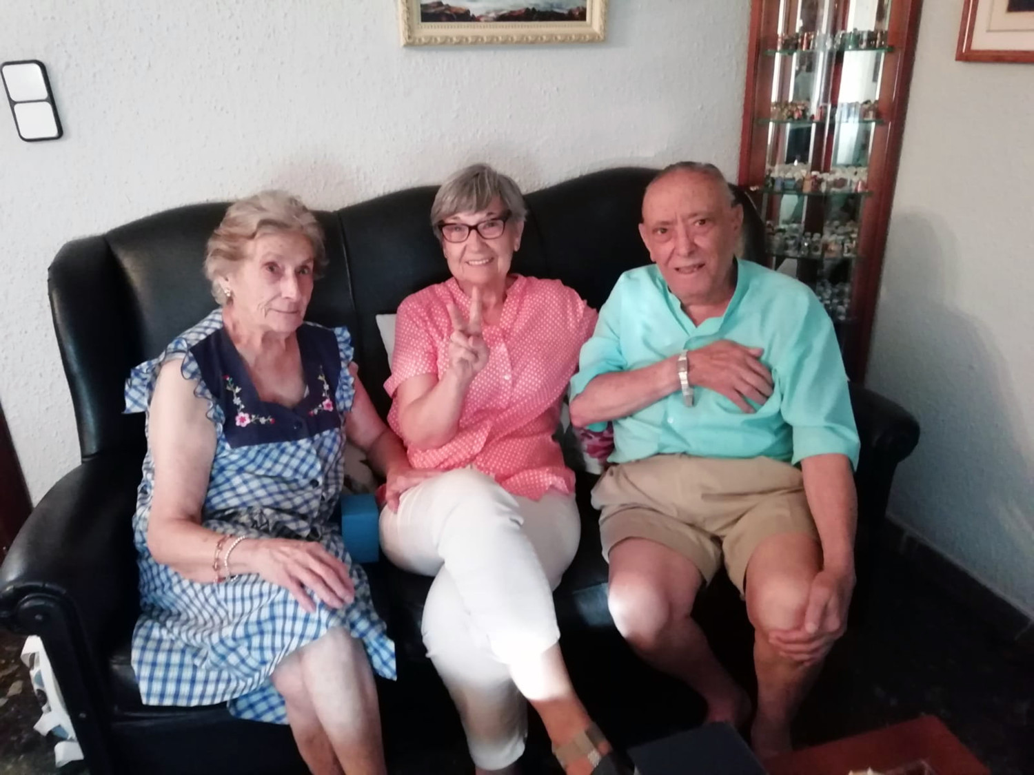 Von rechts nach links beschrieben: ganz rechts sitzt ein älterer Mann, sein Name ist Francisco. Er ist der Großneffe von Cayo und trägt die Armbanduhr von Cayo am rechten Handgelenk. Er hat eine beigefarbene Hose und ein türkisfarbenes T-Shirt an. Francisco sitzt neben zwei Frauen auf einer Couch. Die Frau links neben ihm zeigt ein "Peace"-Zeichen mit der linken Hand. Sie trägt eine weiße Hose und ein rosa gepunktetes Oberteil. Sie hat außerdem eine Brille. Neben ihr sitzt ganz links außen noch eine weitere Frau. Sie hat ein blaues Kleid mit weißen Karo-Muster und Blumenaufdruck an. Alle schauen freundlich in die Kamera.  