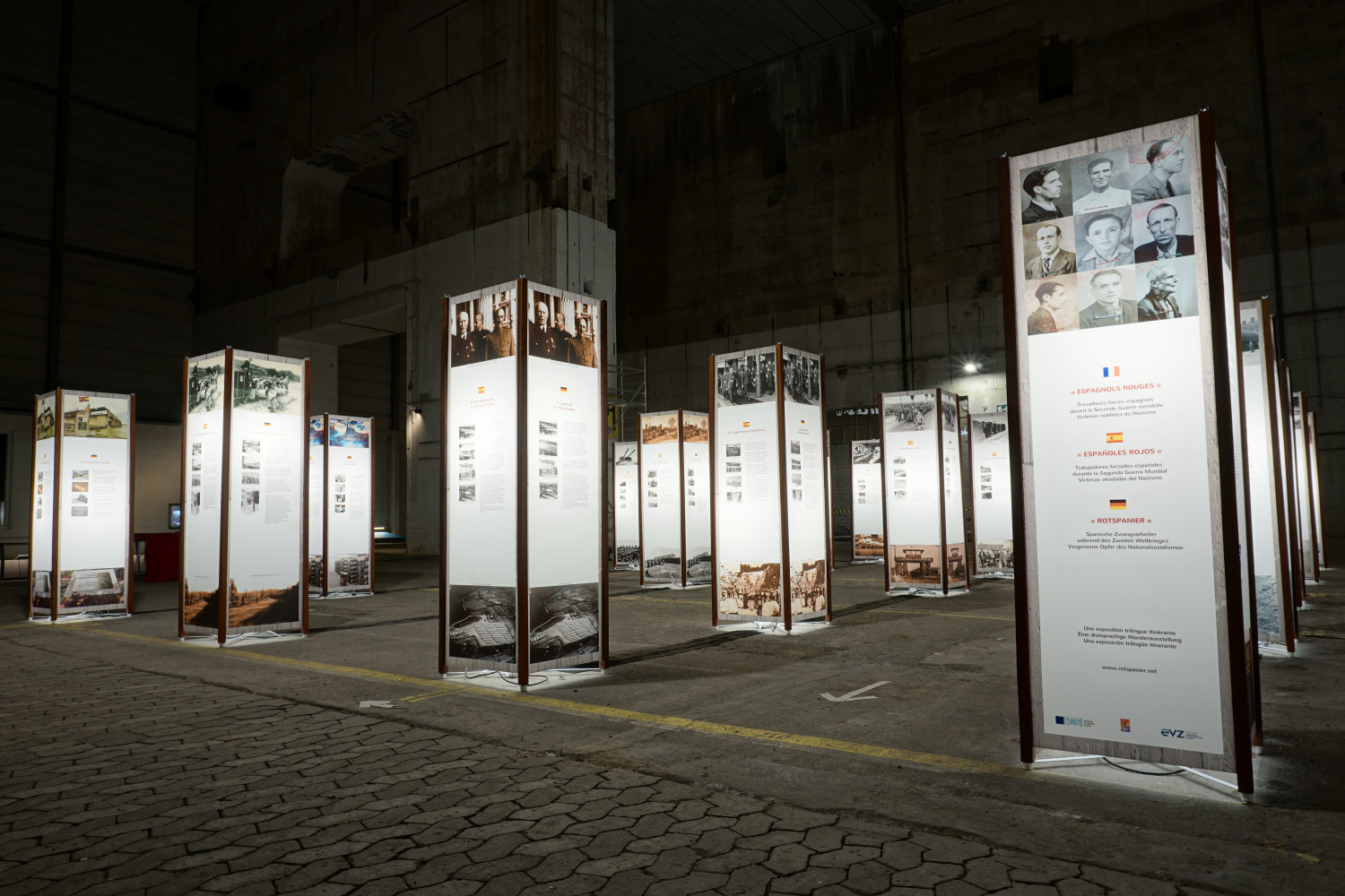 Abgebildet ist das Innere des Bunker "Valentin" mit verschiedenen Balken, die mit Texten und Fotos bedruckt sind. Die Balken sind beleuchtet. Ganz vorne rechts, am äußeren Bildrand, steht ein Balken mit der Aufschrift "Rotspanier", auf französisch, englisch und deutsch geschrieben (von oben nach unten).  