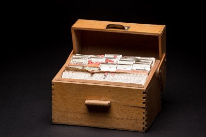 Gezeigt wird eine aufgeklappte, hölzerne Box, welche mit verschiedenen, kleinen Zetteln befüllt ist.