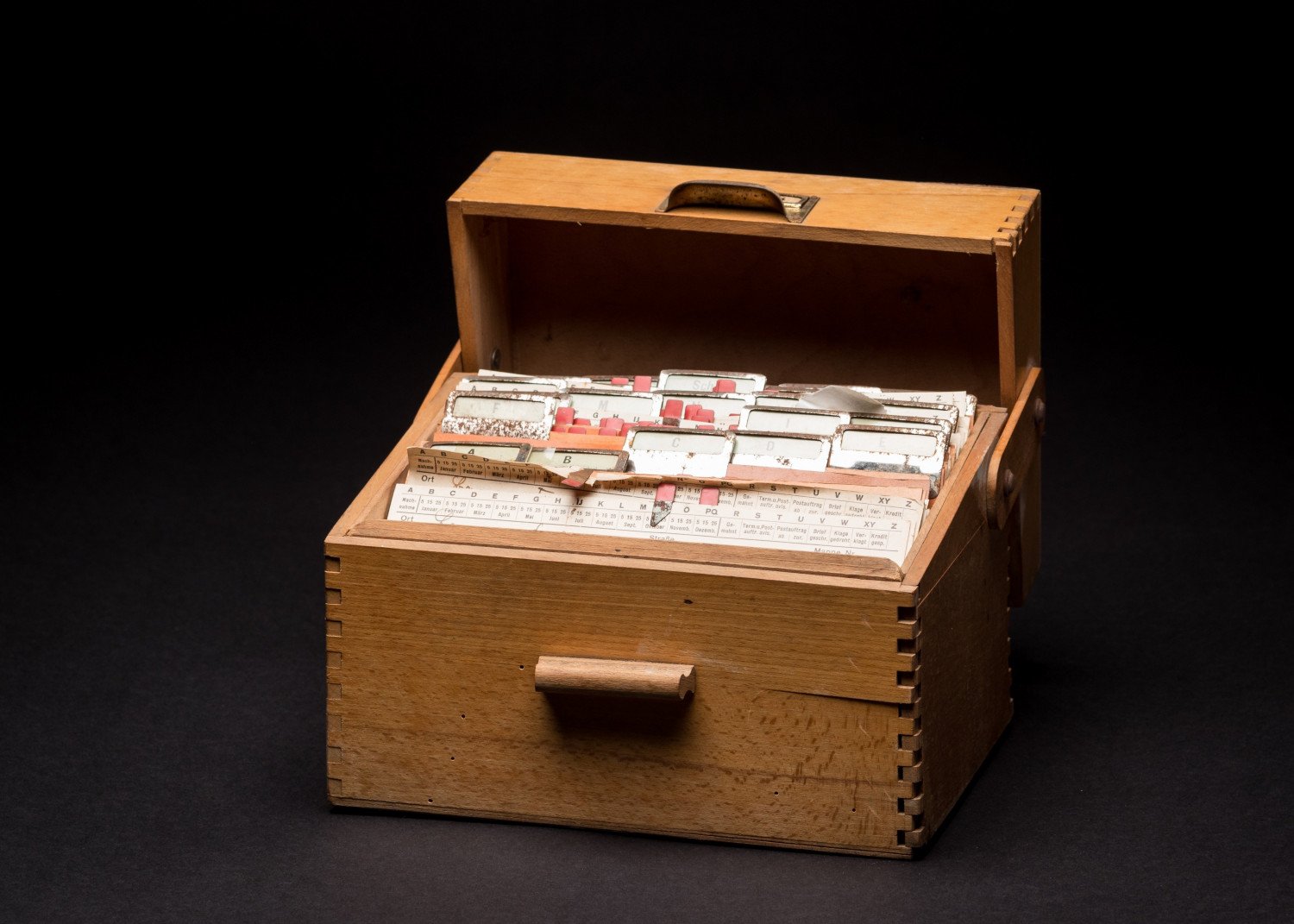 Gezeigt wird eine aufgeklappte, hölzerne Box, welche mit verschiedenen, kleinen Zetteln befüllt ist. 