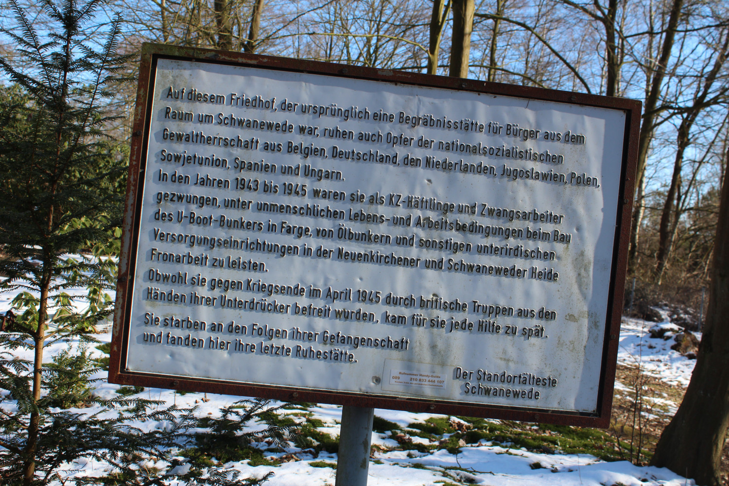 Gezeigt wird eine Tafel mit Inschrift vor einem winterlichen Hintergrund. 