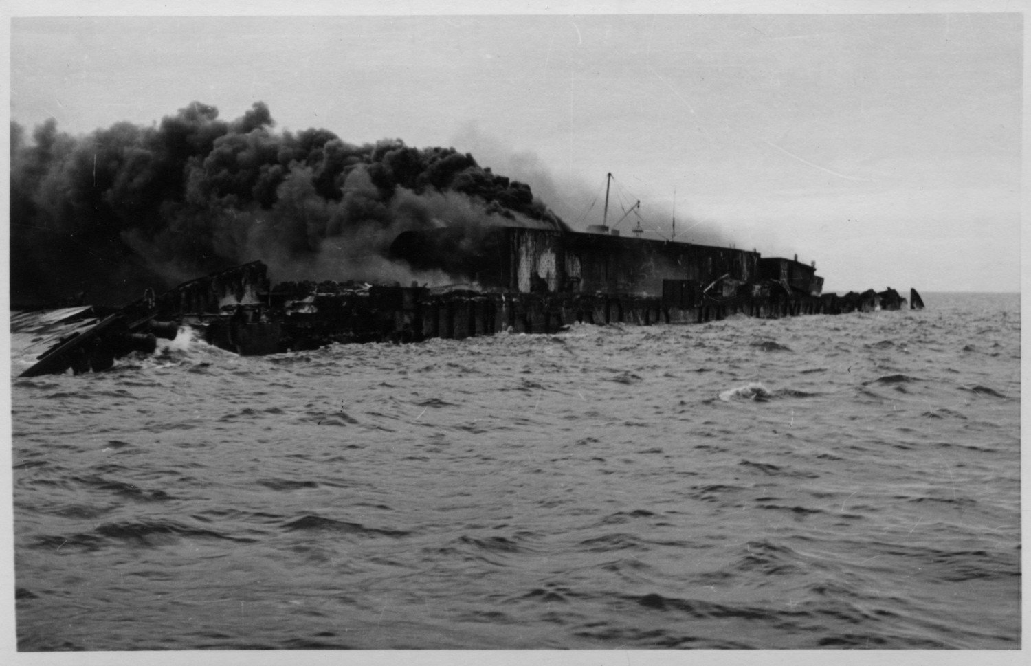 Gezeigt wird ein sinkendes, brennendes Schiff. Es befindet sich (noch) auf dem Wasser. 
