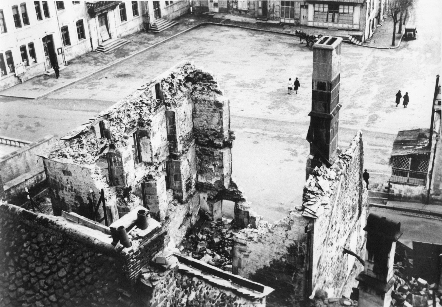 Schwarz-Weiss-Aufnahme aus Vogelperspektive, zerstörte Häuser auf einem Platz. 