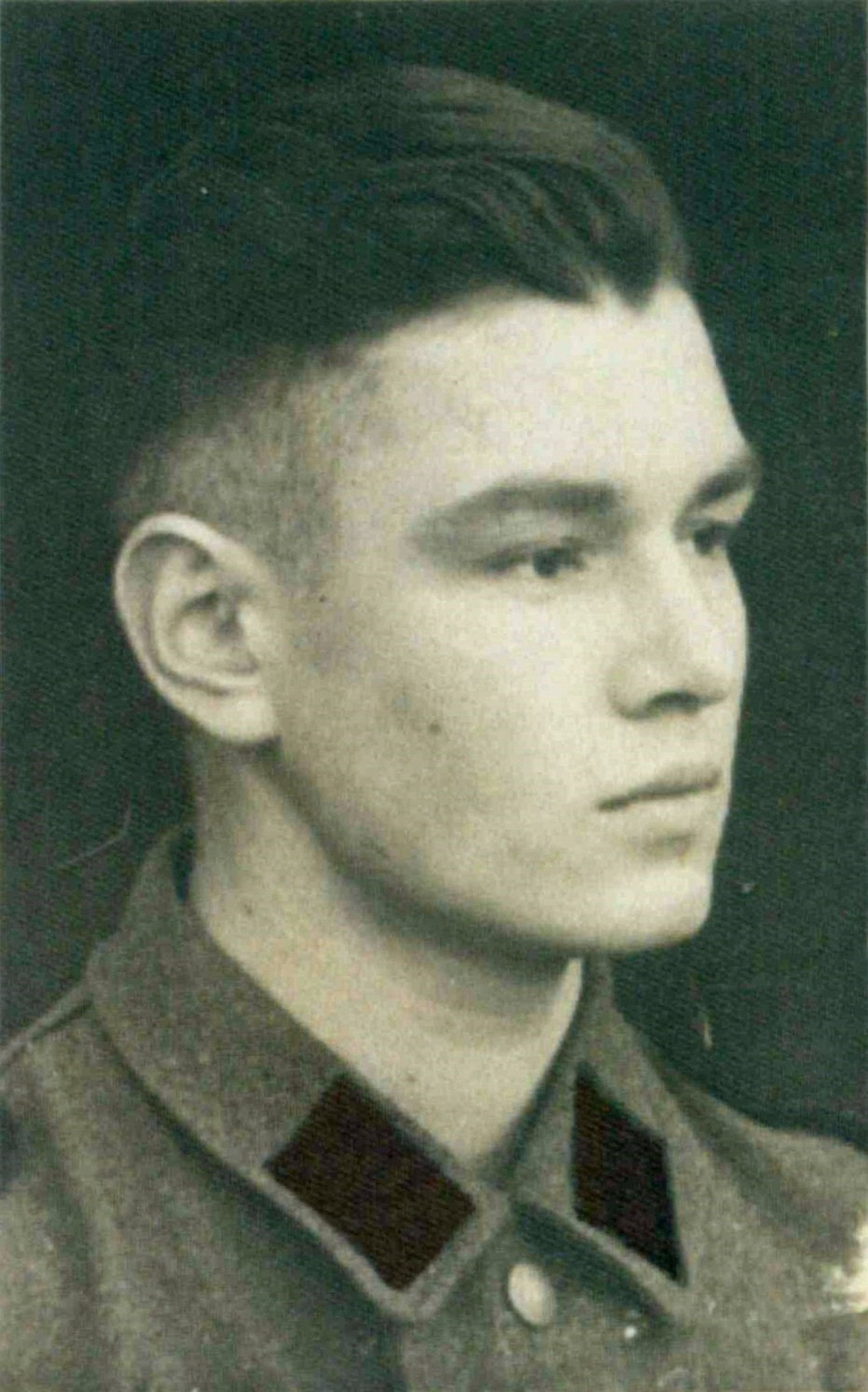 Gezeigt wird eine schwarz-weiß Porträtaufnahme eines jungen Mannes. Er blickt zur Seite, sein Blick ist ernst. Er trägt eine Uniform. 