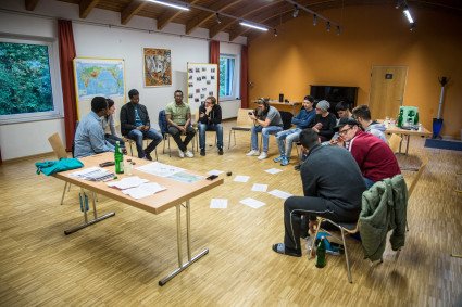 Teilnehmer:innen eines Seminars in der Bildungsstätte Bredbeck sitzen in einem Stuhlkreis. Auf dem Boden zwischen ihnen sind Zettel verteilt.