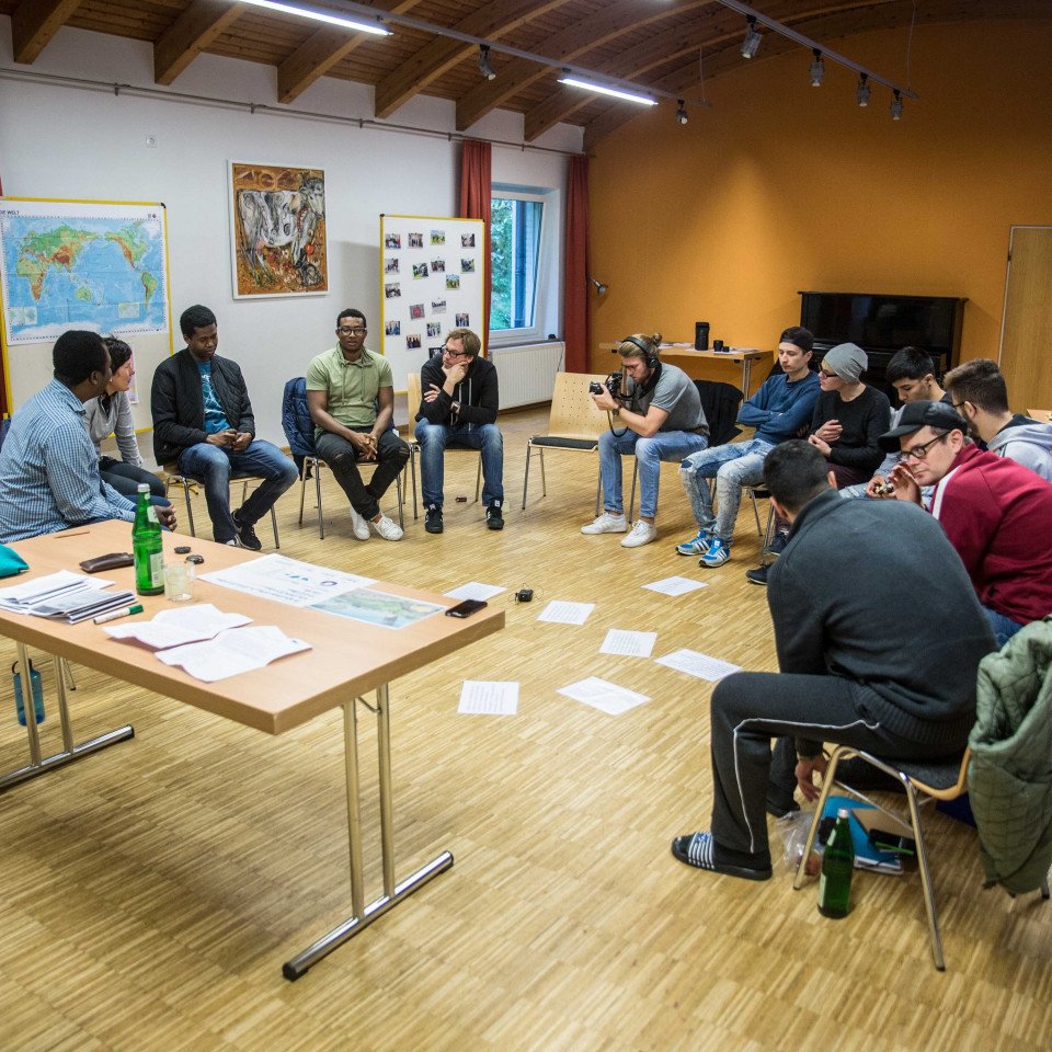 Teilnehmer:innen eines Seminars in der Bildungsstätte Bredbeck sitzen in einem Stuhlkreis. Auf dem Boden zwischen ihnen sind Zettel verteilt.