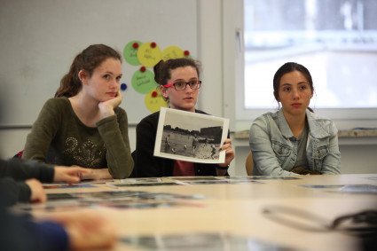 In einem Seminar sitzen drei Teilnehmerinnen an einem Tisch. Eine Teilnehmerin präsentiert ein historisches Foto. Das Foto zeigt Menschen am Strand zur Weser hinter dem Bunker "Valentin".
